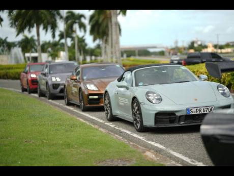 
A lineup of Porsche sports cars takes centre stage in this automotive shot, led by a light gray 911 Turbo S Cabriolet. 