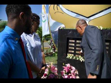 Dr Christopher Tufton (right), minister of health and wellness, points out to Swain Henry and Annakay Henry the name of their father, Patrick Henry, on the monument unveiled yesterday in honour of healthcare workers who died during the COVID-19 pandemic. 