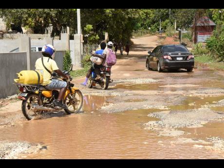 Motorists navigate a pothole-riddled road in Red Berry, Manchester. The potholes are seen filled with water from a burst pipe.