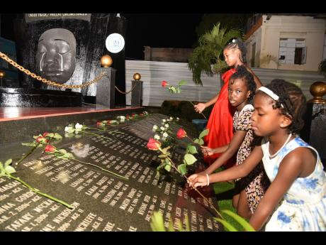 Tyra Falconer (right), Aisha Marriott (centre), and Chriselle Maitland (left), lay roses at the Secret Gardens Monument in downtown Kingston during a Child Month Candlelight Vigil held yesterday in memory of children who have died under violent or tragic c