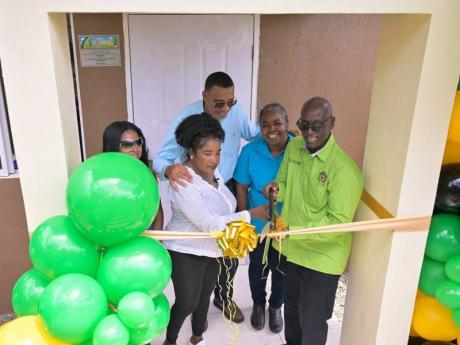 Prime Minister, Dr Andrew Holness (centre), looks on as Minister of Local Government and Community Development, Desmond McKenzie, cuts the ribbon to mark the official handover of a new home to St Thomas resident, Carline Williams (second left). Also sharin