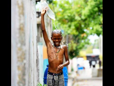 Nine-year-old Nakeifa Page takes a quick shower outside across from his home along Mitchell Street in Kingston on May 17.