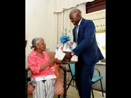 Pearnel Charles Jr (right), minister of labour and social security (MLSS), presents centenarian, Mollie Berkley (left), with a certificate of recognition during the visit which was part of the ministry’s activities to observe National Centenarians’ Day