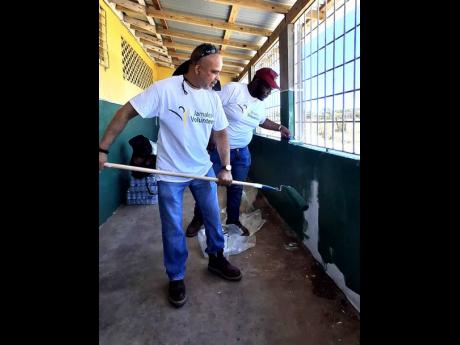 Managing Director Marvin Jackson and other Jamalco volunteers apply paint to a wall on the male dormitory at the Vere Technical High School.