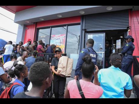 Credit: Antoine Lodge Members of the Jamaica Constabulary Force try to manage the large crowd outside the KFC Rockfort branch in Kingston.