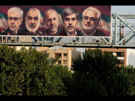 A man walks past a billboard displaying images of top Iranian commanders and scientists killed in Israeli strikes early Friday, in Tehran, Iran, Friday, June 13.