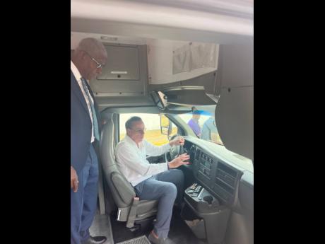 Credit: Photo by Andre Williams Daryl Vaz (seated), minister of science, energy, telecommunications and transports, shows off one of the 110 used buses that will make up the fleet of the National Rural Bus Service while Owen Ellington, managing director of the Jamaica Urban Transit Autho
