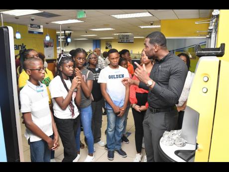 Ricardo Williams (right), head of branch sales and relationship management, gives participants a tour of JN Bank Half-way Tree last year as part of the field trip from the summer camp.