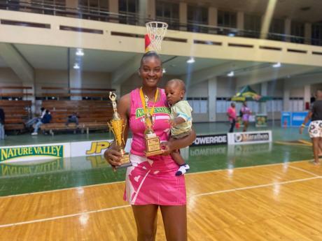 Kingston Hummingbirds’ Tracyann Francis, son in tow, displays the trophies she earned after her team beat the Manchester Spurs in the final of the Red Strip Flavours Netball Jamaica Elite League at the National Arena on Sunday. 
