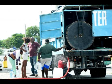 In this 2020 photo, people are seen filling water in containers from a water truck in Denham Town.
