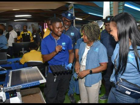 Minister of Education, Skills, Youth and Information, Senator Dr Dana Morris Dixon (centre), listens as Dihanroy Mitchell of the HEART/NSTA Trust highlights features of the agency’s technology display at the Denbigh Agricultural, Industrial and Food Show