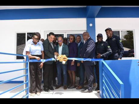 Deputy Prime Minister and Minister of National Security Dr Horace Chang (4th from left) is being assisted by Homer Davis, member of parliament for St James Southern (3rd from left), to cut the ribbon for the official opening of the new Anchovy Police Stati