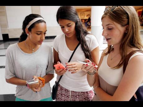 Isabella Cimato, 17 (from left), Arianna Schaden, 4, and Sofia Harrison,15, check their phones at Roosevelt Field shopping mall in Garden City, NY.