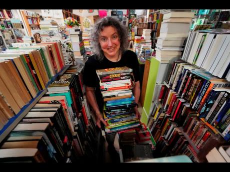 Michelle Souliere, owner of the Green Hand Bookstore, carries a stack of books to the shelves, in Portland, Maine.