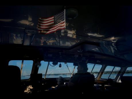 An American flag is reflected in the windows of the bridge as mate Peter Emery pilots the Gaspee, a crew transport vessel, along the Sakonnet River near Portsmouth, Rhode Island, during the eight-hour trip to the Liftboat Robert platform and Expedition 501