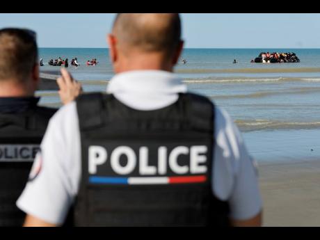 French police officers take photos of migrants as they board a small boat to reach Britain, in Gravelines, northern France.