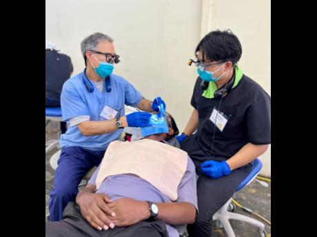 Dr Mark Stevenson (left), a dental practitioner with 34 years of experience, performs a root canal on a faculty member at William Knibb Memorial High School as part of the Great Shape! Inc. 1000 Smiles Mission, hosted at the school. Assisting him is Daniel