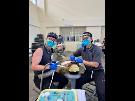 Dental practitioners Andrew Lim (left) and Ryan Elido flash masked smiles for the camera as they clean a patient’s teeth during the Great Shape! Inc. 1000 Smiles Dental Mission, held recently at William Knibb Memorial High School in Trelawny.