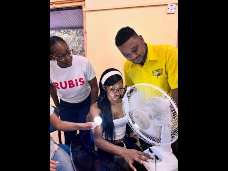 A SCATE camper powers on a solar fan reassembled during a hands-on renewable energy session led by facilitator Paul Russell, head of energy solutions at ISRATECH. Looking on is Alyssa Jolly, as the activity unfolded at the UWI Faculty of Engineering. 
