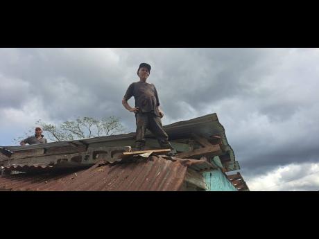 Credit: Photo by Gareth Davis Sr Edwin Thompson stands atop the roof of his home in Portland on Thursday, after it was damaged by Hurricane Melissa.