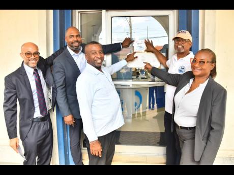 Michael McMorris (second right), chair of the Downtown Kingston Redevelopment Initiative Committee, affixes the decal on the door of Imperial Optical Broadbent on Duke Street. Sharing in the moment on Wednesday are (from left) Jonathan Swire, second vice-p