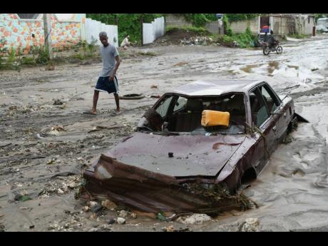 A pedestrian looks at a flooded car in the aftermath of Hurricane Melissa in Petit-Goave, Haiti, Thursday, October, 2025. 