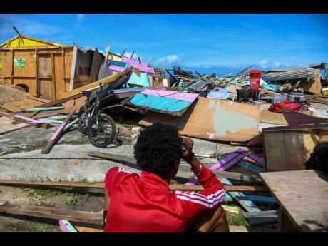 On October 29, a fisherman of Salem in St Ann sits among the rubble holding his head in despair as he looks on at the damage done to the shacks on the Salem fisherman's beach in St Ann.