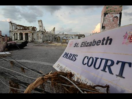 A toppled Black River Courthouse sign lies before damaged historic buildings on High Street, a stark symbol of the town’s battered heritage after Hurricane Melissa.