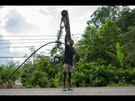 Richard Edwards walks past a downed light pole and dangling wires along the Enfield main road in St Mary.