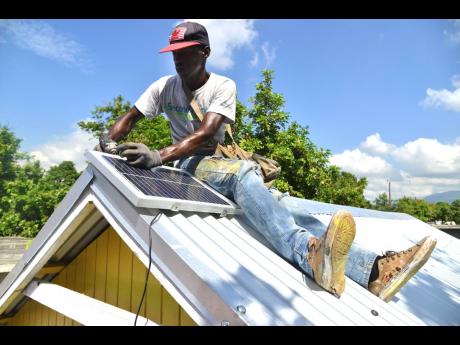 Demar Banton a carpenter working with Food For The Poor installs a solar panel on the roof of a newly bult house for a family in Kingston.