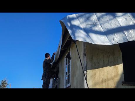 A member of the JDF assists with the laying of a tarpaulin on a roof in Granville, Trelawny last week