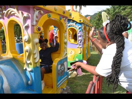 Keisha Sutherland (right), waves to her daughter Shakeira Morris (left) as she rides on the train at the Funland at Hope Gardens in St Andrew during the Digicel Foundation Christmas Treat for special needs children yesterday.  