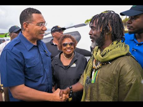 Prime Minister Dr Andrew Holness (left) with Chief of the Accompong Maroons in St Elizabeth, Richard Currie, during a visit to the community. Olivia Grange, minister of culture, gender, entertainment and sport, looks on.