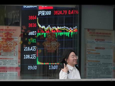 AP
A woman passes by a stock index at a brokerage in Beijing in May 2025. 