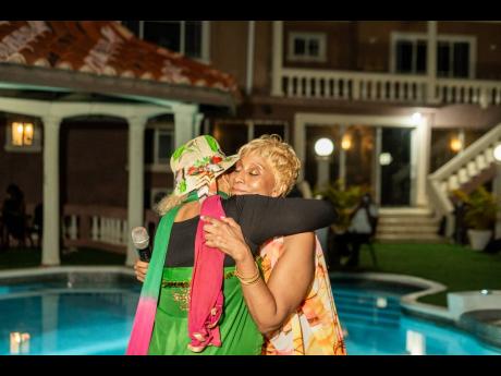Dr Marcia Griffiths (left) shares a warm embrace with fellow reggae songstress Nadine Sutherland during the postgraduation reception at her home, moments after Sutherland delivered a moving tribute in honour of the newly conferred cultural icon.