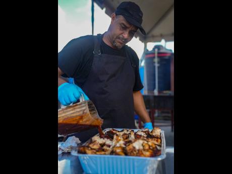 Credit: File Chef Donald Pallas adds rich jerk sauce over fresh chicken in the packing section of the Negril Field Kitchen, locking in the smoky spice that defines this iconic dish. “The sauce rounds it all out,” he says. “That’s what makes it finger-licking go