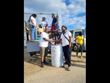 Chief Executive Officer of the Croydon Black Minority Ethnic (BME) Forum, Dr Andrew Brown (left), hands over a barrel of tools and building supplies to community members Michael (centre) and Ridge Harvey (right) in Parottee, St Elizabeth, on January 22. Th