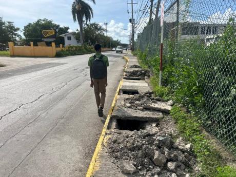 Credit: Photo by Mickalia Kington The crumbling sidewalk in front of the National Works Agency office along Barracks Road in Savanna-la-Mar, Westmoreland, forces this student to walk on the road surface.