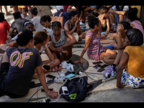 Residents charge their electronic devices on a street during a general blackout in Havana, Saturday, March 15, 2025. 