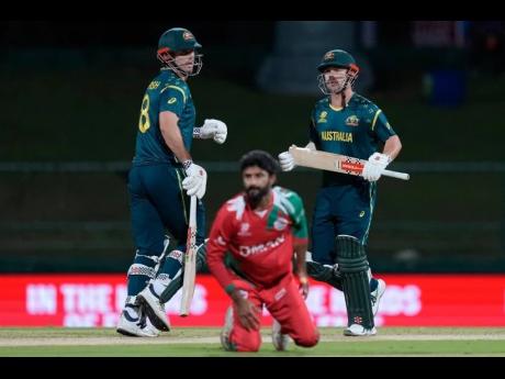 Australia’s Travis Head and captain Mitchell Marsh run between the wickets as Oman’s Jay Odedra (centre) dives to field a ball during the T20 World Cup cricket match between Australia and Oman in Pallekele, Sri Lanka, yesterday.