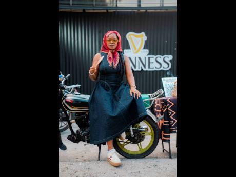 Reggae artiste Khalia sits pretty, rocking a flared denim midi dress, coloured specs and a red head scarf as she keeps cool with a hand-held fan.