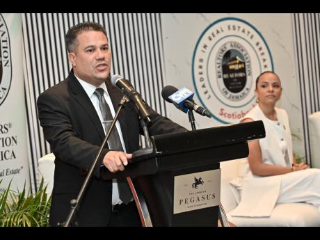 
Matthew Samuda, minister of water, environment, and climate change, speaks while Gabrielle Gilpin-Hudson, (right) president of Realtors Association of Jamaica, looks on at the Realtors Association of Jamaica Leaders in Real Estate Breakfast under the them
