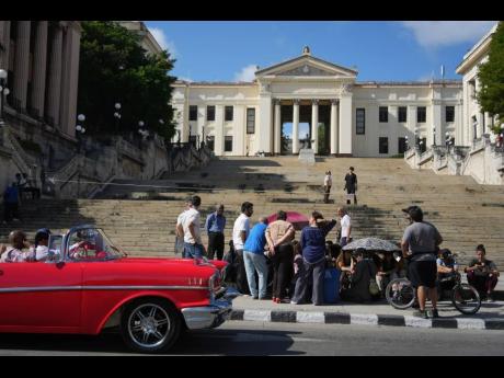 A car rides past students sitting outside the University of Havana during a protest over an energy crisis that has disrupted classes in Havana, Cuba, Monday, March 9, 2026. 
