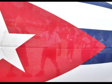 Children are seen through the Cuban flag while they walk to the Havana's Malecon to toss flowers into the ocean in commemoration of the anniversary of the death of the Cuban revolutionary Commander Camilo Cienfuegos on October 28, 2004 in Havana, Cuba. (AP