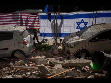 Israeli authorities hang Israeli and United States flags at the site struck by an Iranian missile that killed two people, in Ramat Gan, Israel on March 18, 2026. (AP Photo/Oded Balilty)