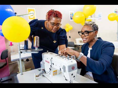 State Minister in the ministry of National Security and Peace, Juliet Cuthbert-Flynn (right), is being assisted by Chief Technical Director in the ministry, Shauna Trowers, with threading a sewing machine in the new sewing lab at the South Camp Juvenile Co