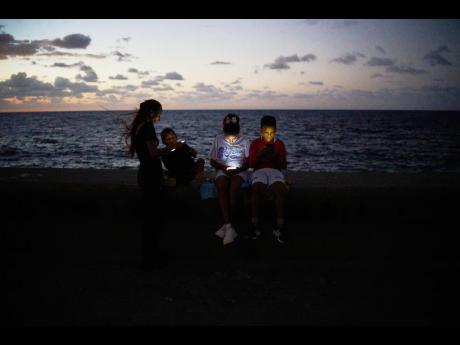 Children look at their phones while sitting on the Malecón wall during a blackout in Havana, Cuba.