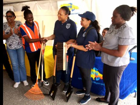 President of the Majesty Gardens Community Development Corporation, Jaheim Mitchell (second left), receives cleaning tools from Pan American Development Foundation Project Coordinator, Kimberly Seymour-Brown, at the Community Clean-up, E-Waste Drive, and t