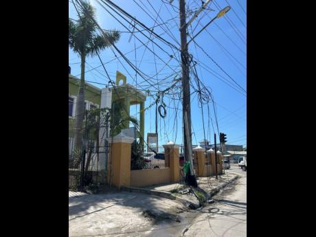 Low-hanging cables drape across a sidewalk at Dunbar’s River in Savanna-la-Mar, forcing pedestrians into the busy roadway and raising safety concerns.