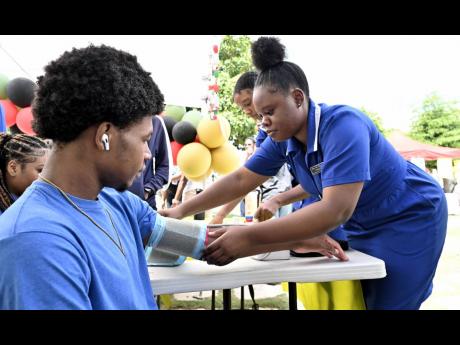 Nursing students Ashanti Mootie (right) check Tajay Fuller’s blood pressure during the College of Health Sciences’ annual health fair, held yesterday at UTech’s campus in St Andrew. 